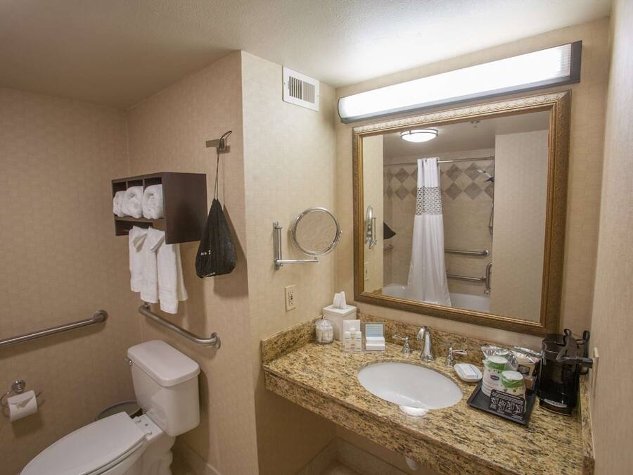 A bathroom with a toilet, sink, and mirror. There are towels and toiletries on the counter.