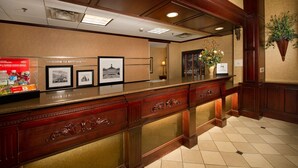 A reception desk with framed pictures, a welcome sign, and a plant. - Hampton Inn & Suites Stillwater (Stillwater)