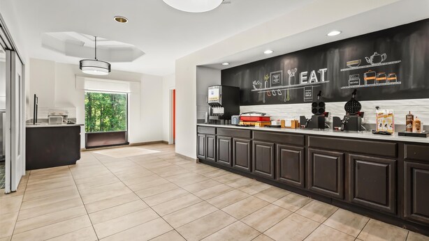 A modern kitchen with dark cabinetry, a large island, and a black backsplash with 'EAT' and food-related graphics. - Hampton Inn Elkton (Elkton)
