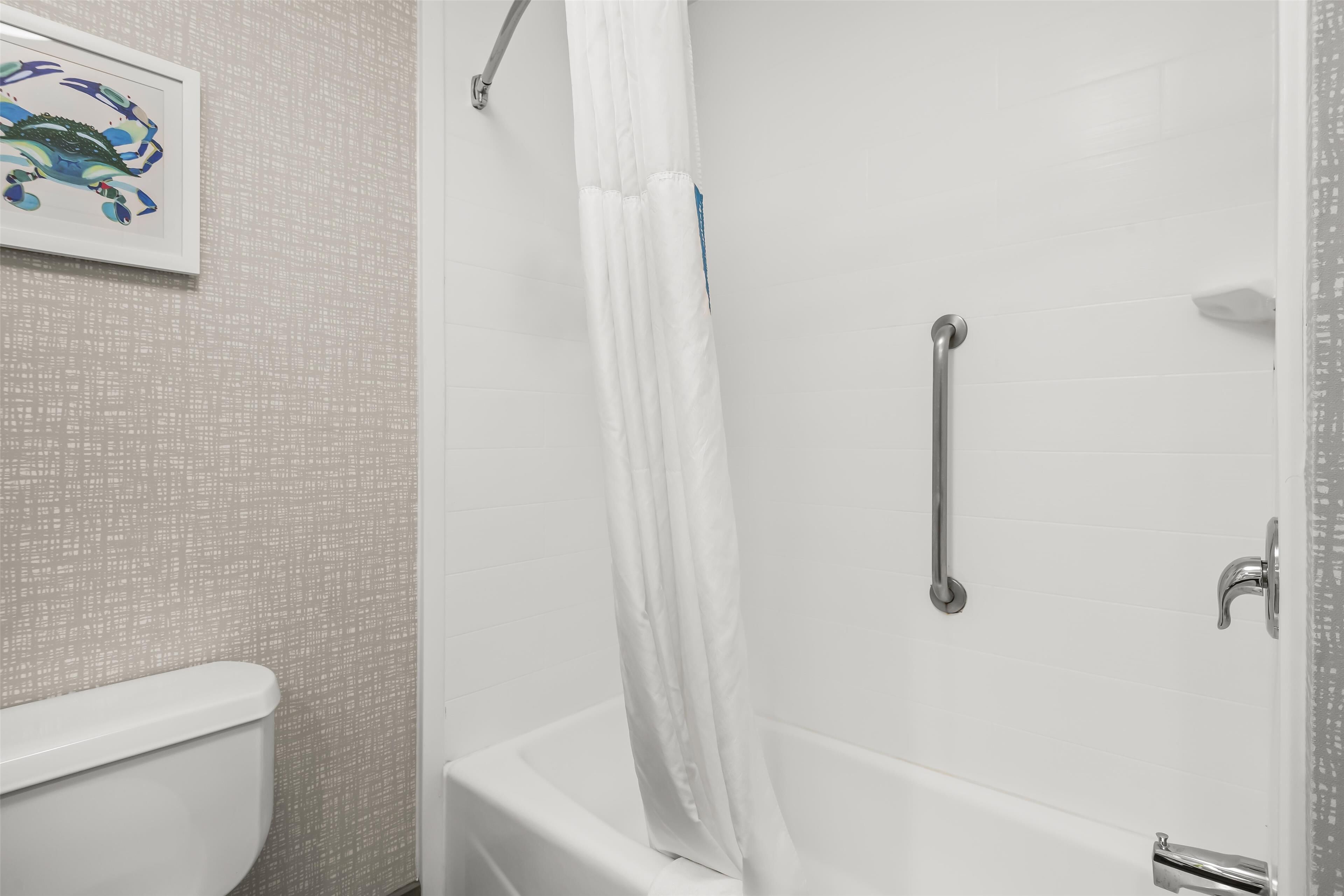 Un baño con una bañera blanca, una cortina de ducha, un asidero y un cuadro en la pared.