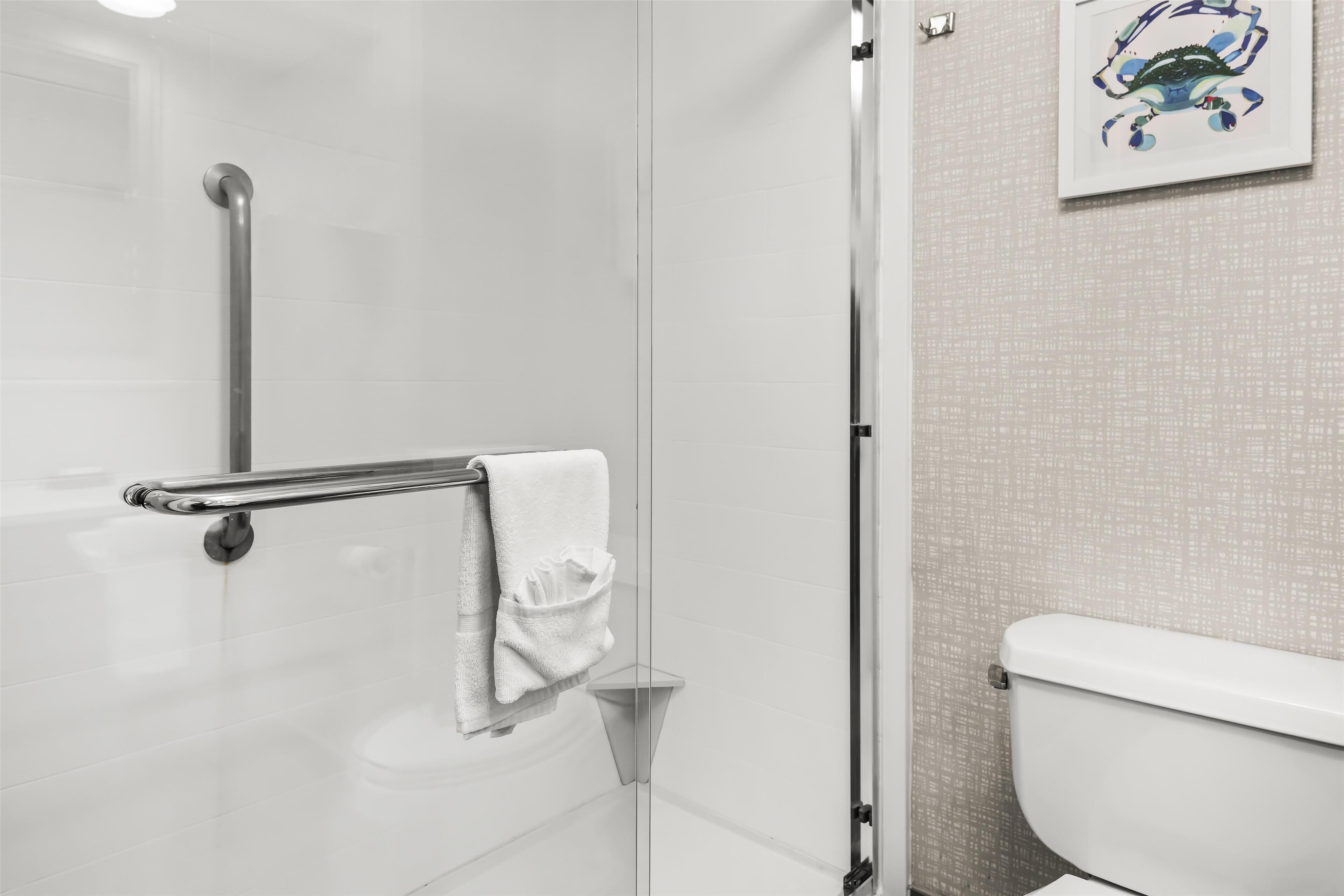 A bathroom with a glass shower enclosure, a white toilet, and a towel rack with a white towel.