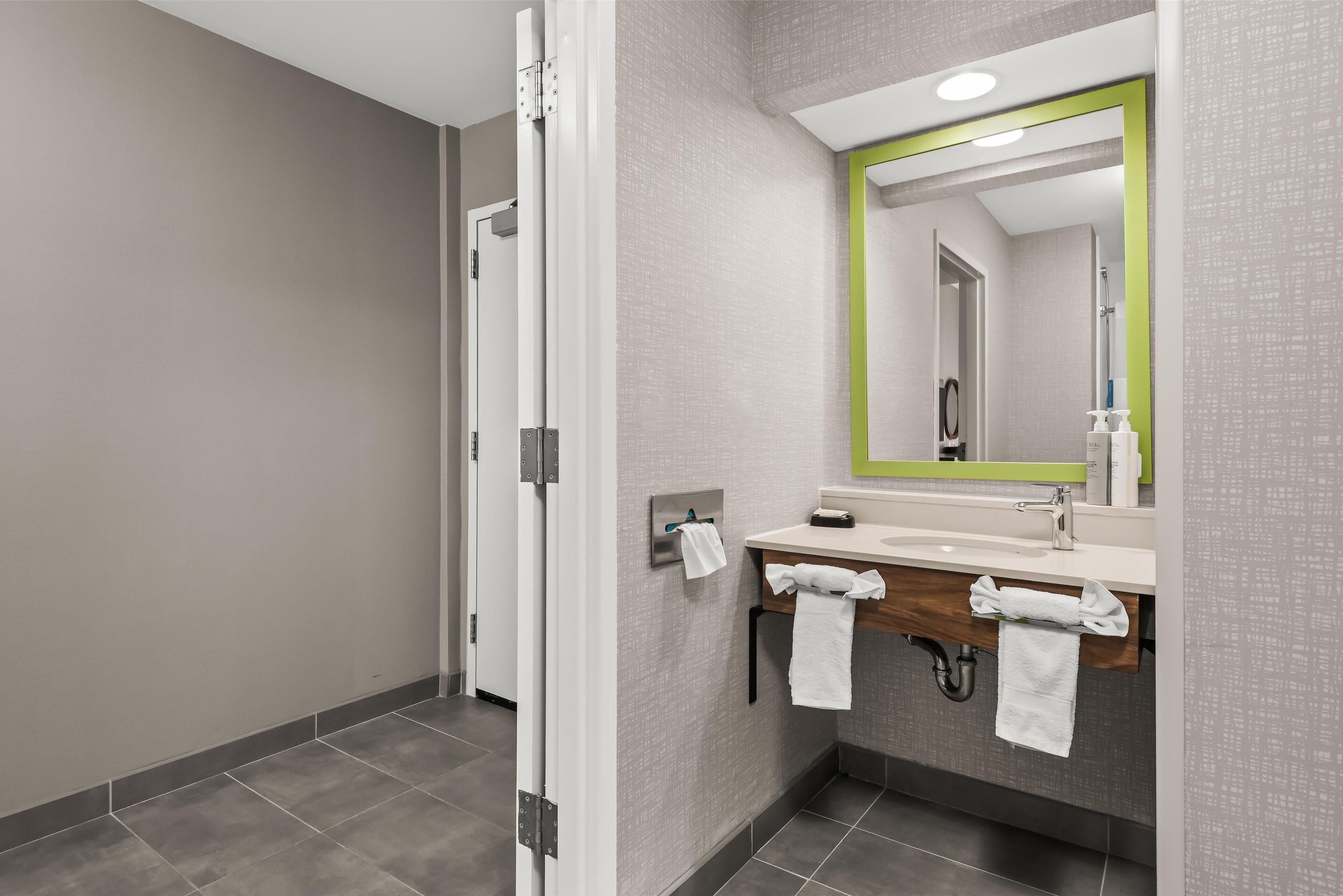 A modern bathroom with a shower, a sink with a mirror, and towels hanging on hooks.