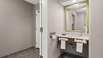 Un baño moderno con ducha, un lavabo con espejo y toallas colgadas en ganchos.