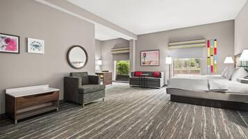 A modern hotel room with a bed, a sofa, a desk, and a bathroom vanity.
