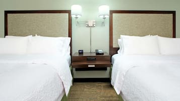 A hotel room with two beds, a nightstand, a lamp, and a mirror.