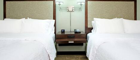 A hotel room with two beds, a nightstand, a lamp, and a mirror.