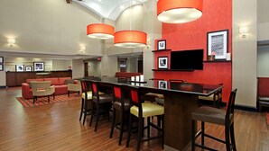 Un lobby amplio con techo alto, una zona de bar central con taburetes, un sofá y un televisor montado en la pared.