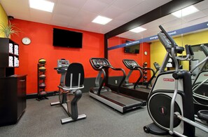 Une salle de sport équipée de tapis de course, de vélos elliptiques et d’une horloge murale.
