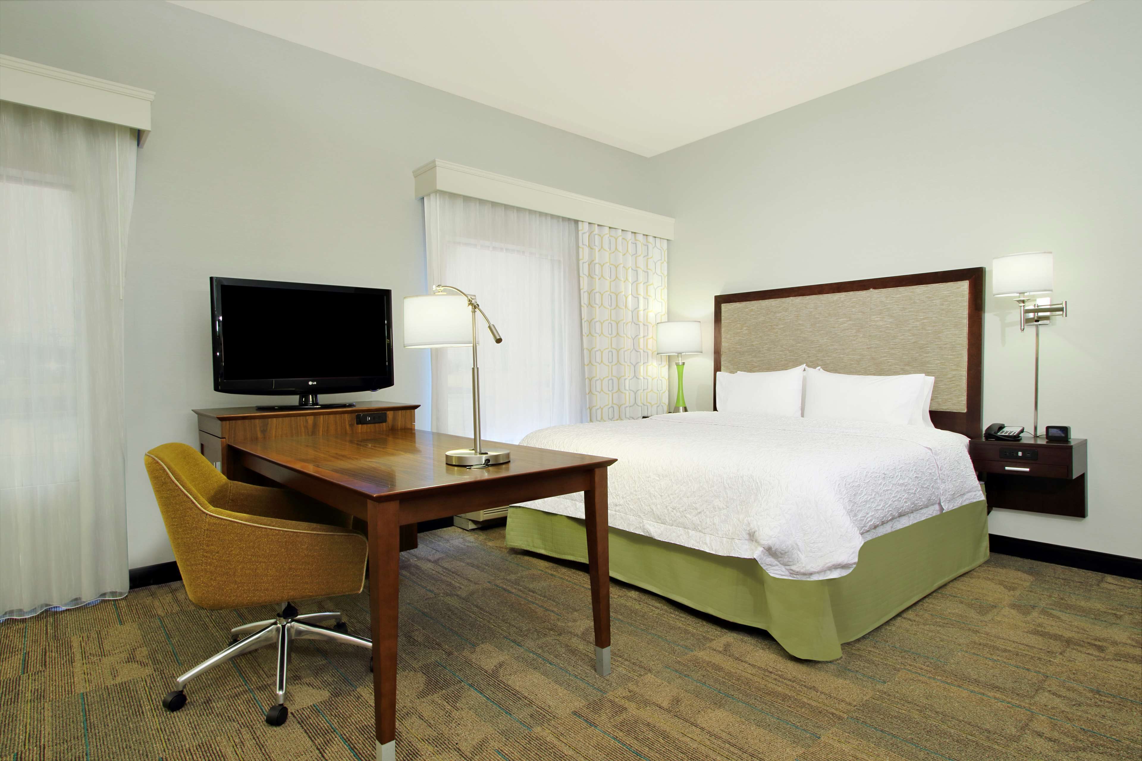 A hotel room with a bed, a desk with a television, a chair, and two bedside lamps.