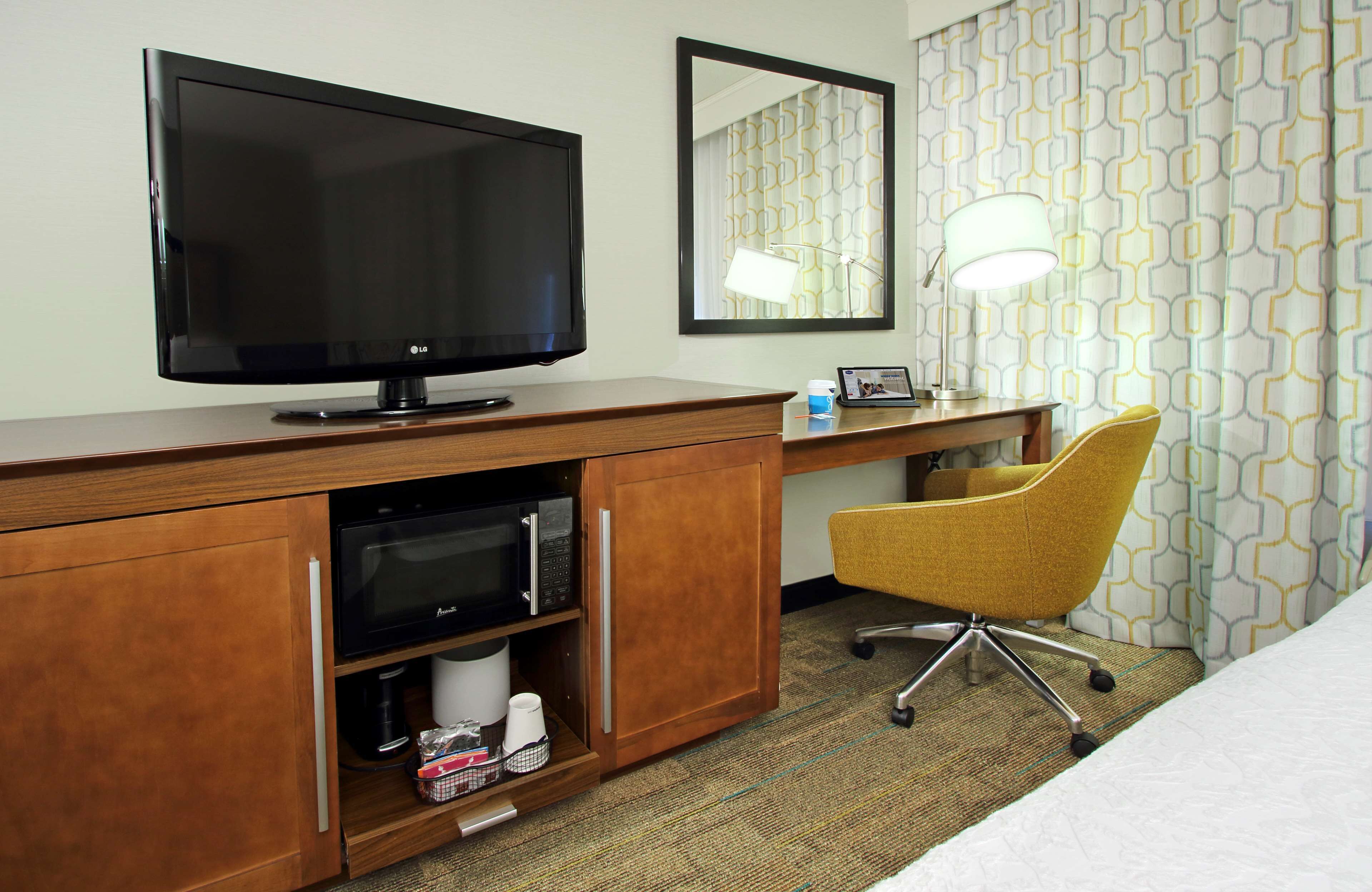 Une chambre d’hôtel avec une télévision, un bureau avec une lampe, une chaise jaune et un lit.