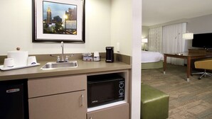 Habitación de hotel pequeña con kitchenette, una cama, un escritorio y televisor.