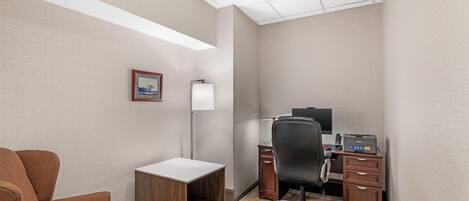 A hotel office room with a desk, chair, lamp, and a framed picture on the wall.