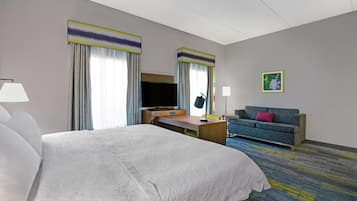 Habitación de hotel con una cama grande, un escritorio, un televisor, un sofá y un cuadro en la pared.