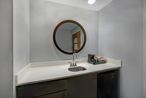 A bathroom with a white sink, a round mirror, and a coffee maker on the counter. - Hampton Inn & Suites Augusta West (Augusta)