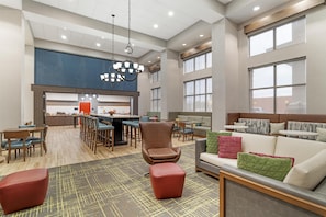A spacious hotel lobby with a dining area, seating arrangements, and a kitchenette.