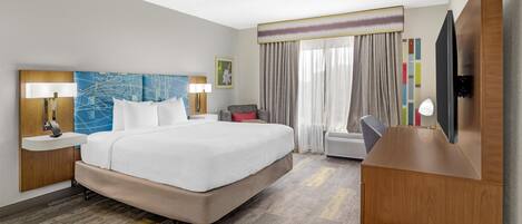 Een hotelkamer met een groot bed, een bureau, een stoel, een televisie en een raam met gordijnen.