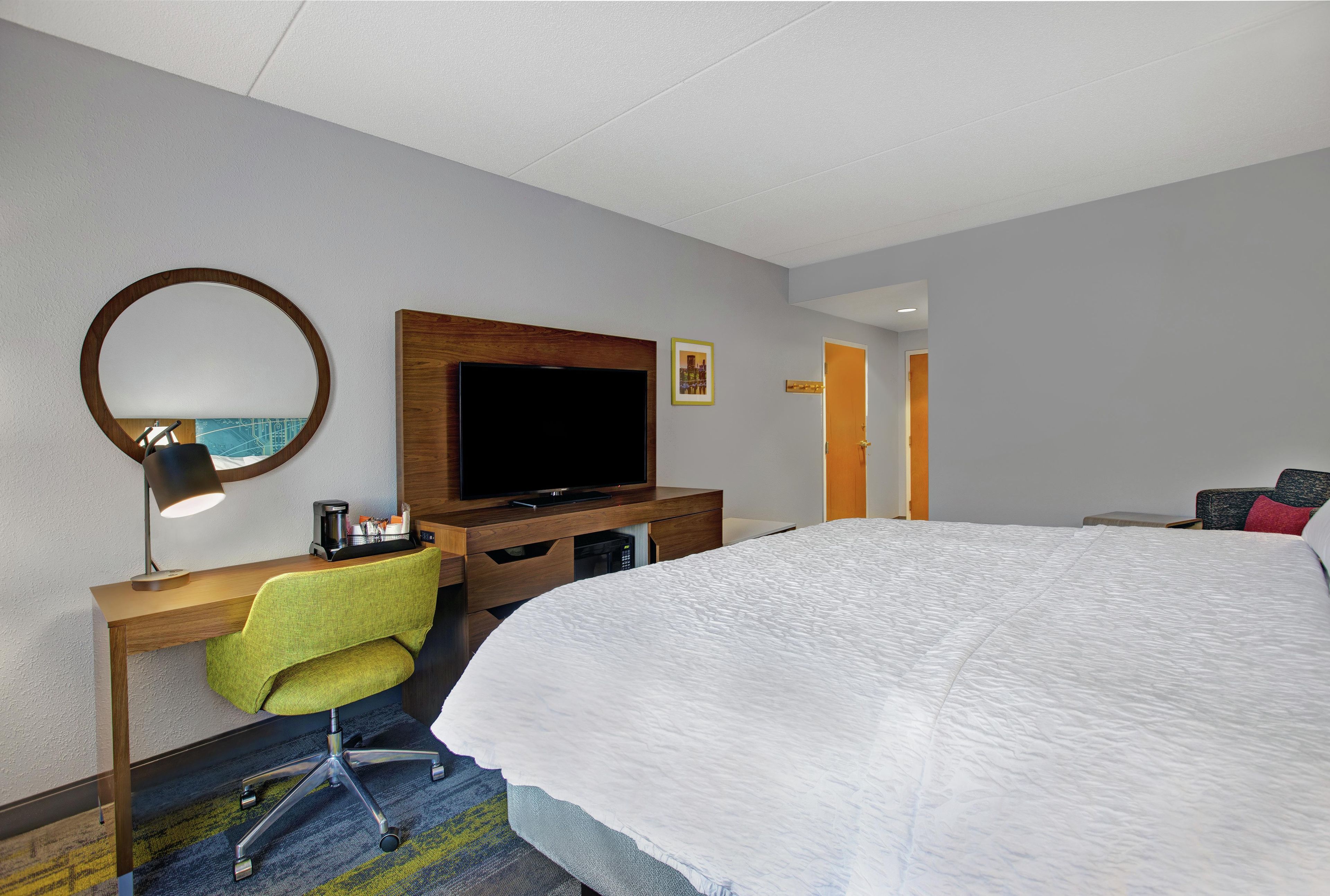 A hotel room with a bed, a desk with a chair, a television, and a mirror.