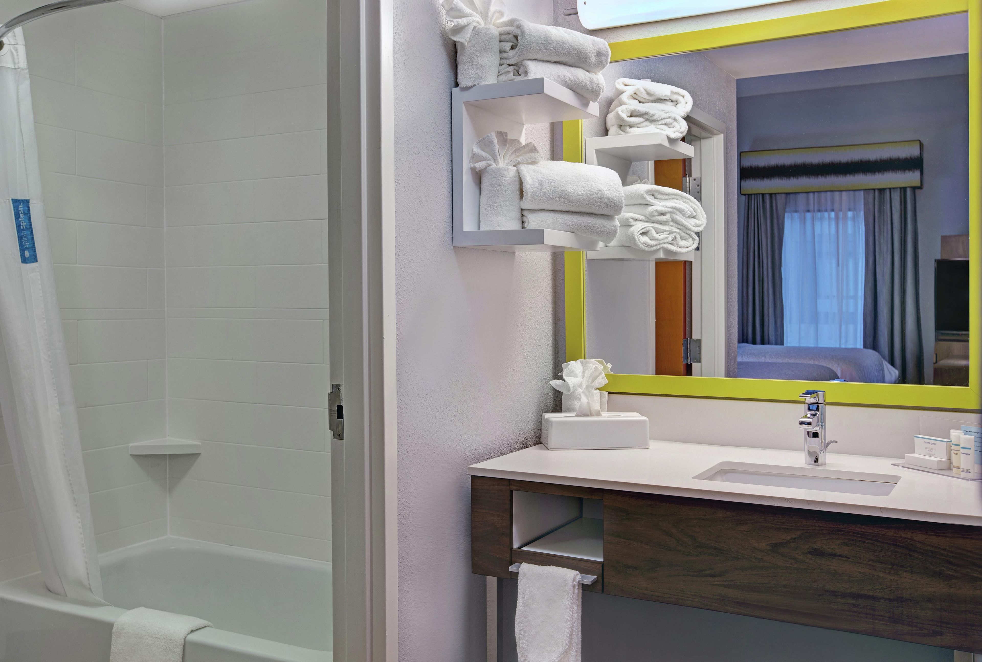 A bathroom with a shower, a sink, a mirror, and towels.