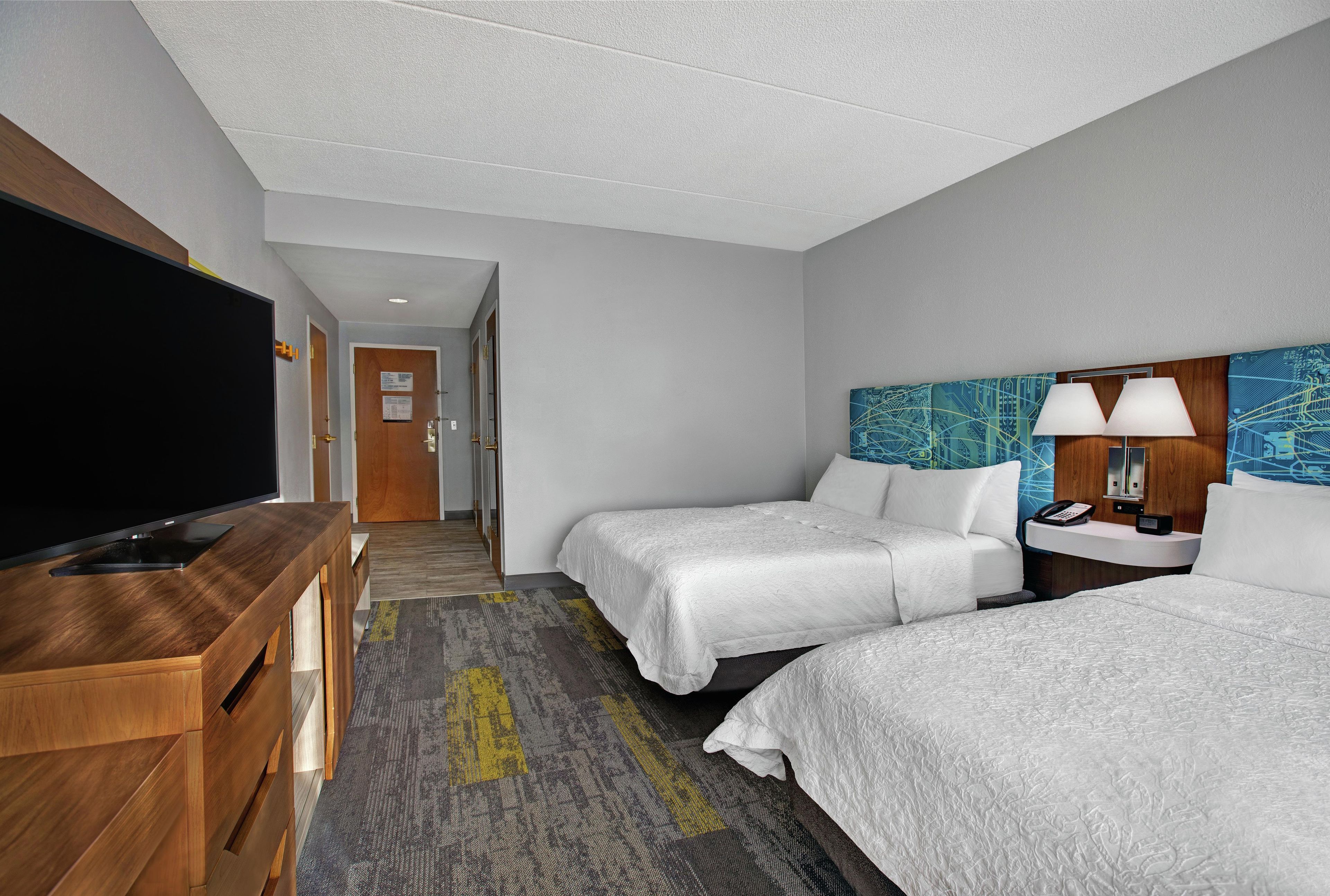 A hotel room with two beds, a TV, a desk, and a bathroom.