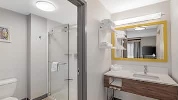 Un baño moderno con cabina de ducha de vidrio, un lavamanos blanco sobre un mueble de madera y un espejo con marco amarillo.