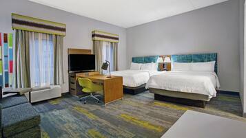 A hotel room with two beds, a desk, a chair, a TV, and an air conditioning unit.