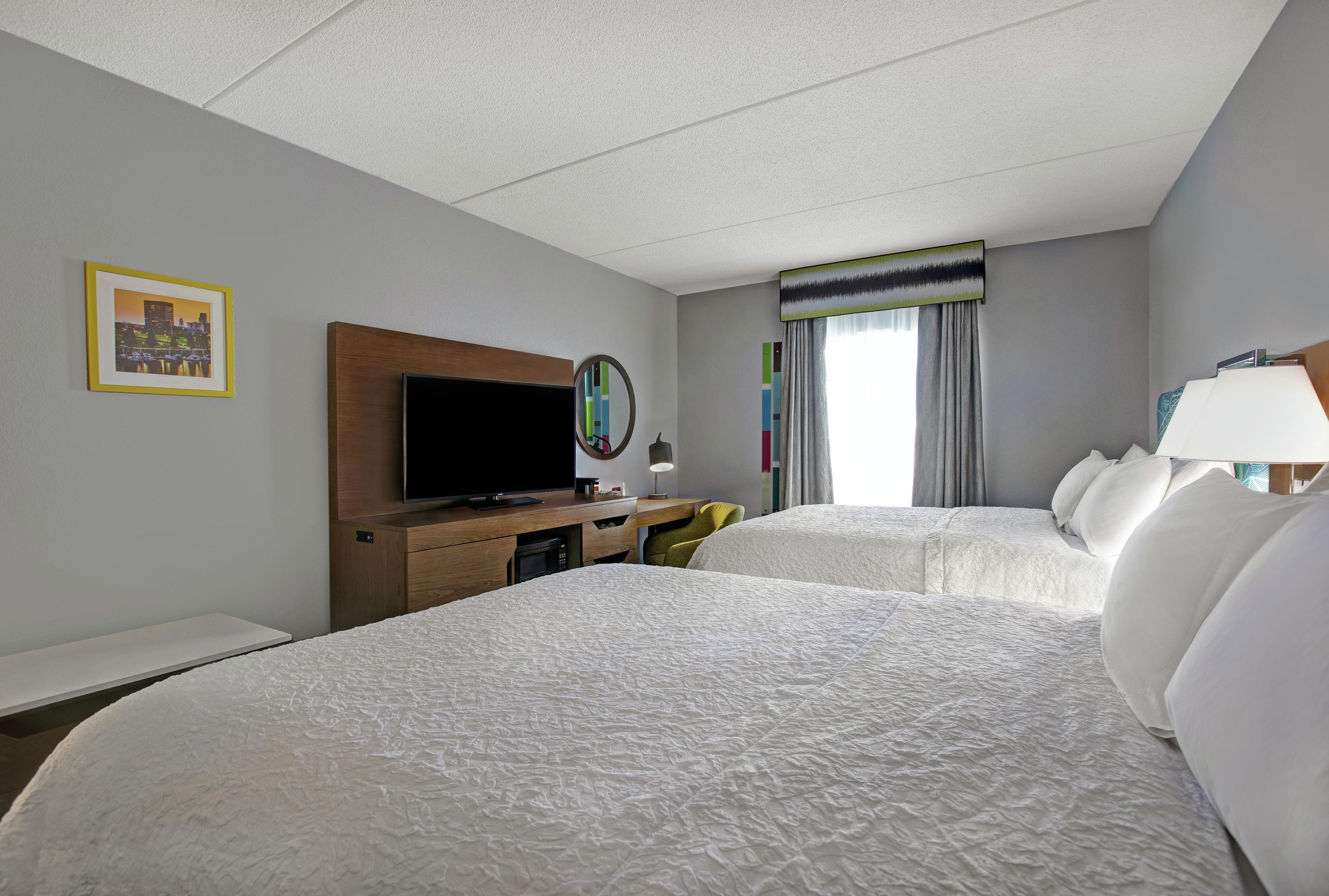 A hotel room with a large bed, a television, a desk, and a window with curtains.