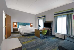 A hotel room with a bed, desk, TV, and a large window with curtains.