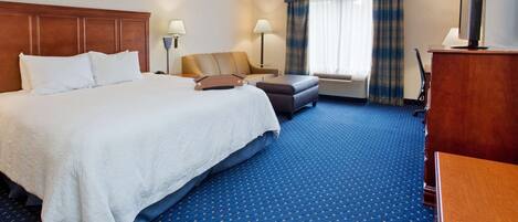 A hotel room with a large bed, a desk, a chair, a TV, and a window with curtains.