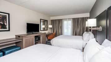 Una habitación de hotel con dos camas, un escritorio con computadora, televisor y una silla.