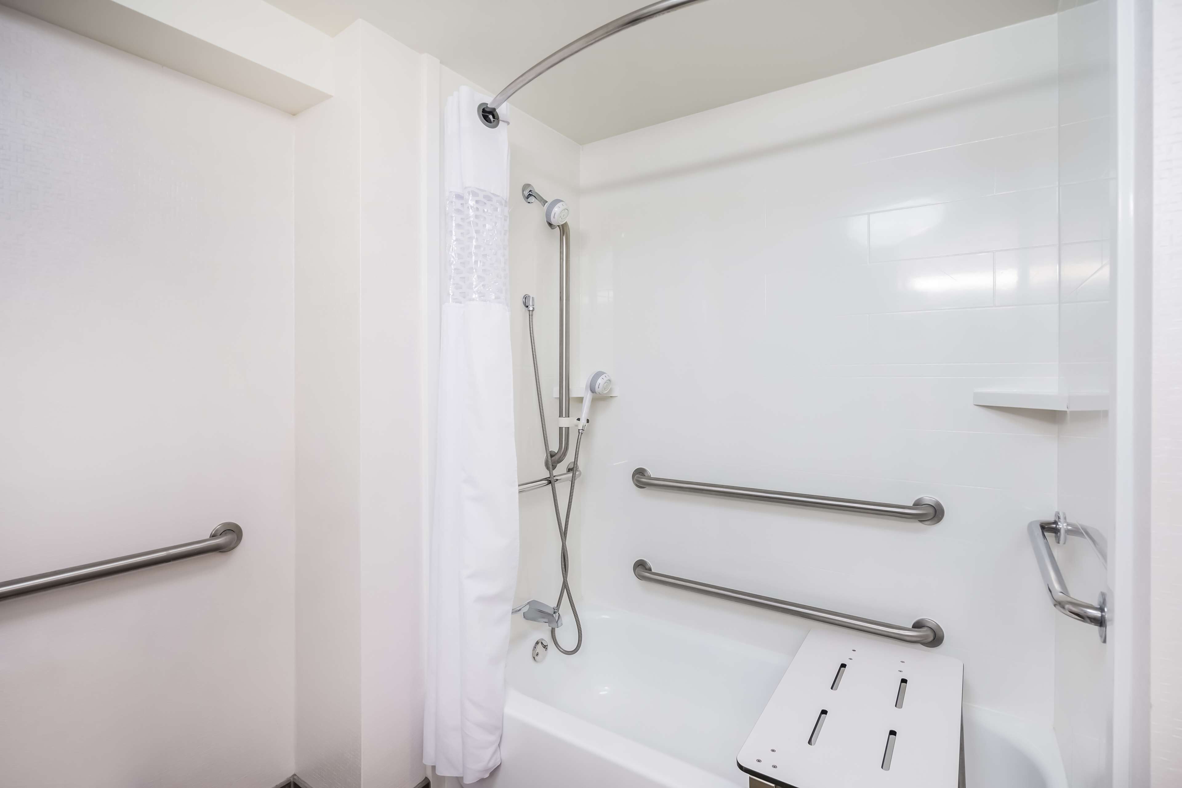 Une salle de bain moderne dotée d’une douche à l’italienne, de barres d’appui et d’une baignoire.