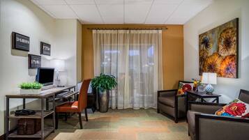 A hotel room with a desk, chair, sofa, and a large window with sheer curtains.