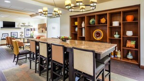 A modern dining area with a long table, multiple chairs, and a decorative shelf with various items.