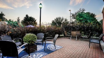 An outdoor patio with brick flooring, wicker furniture, and a patterned rug.