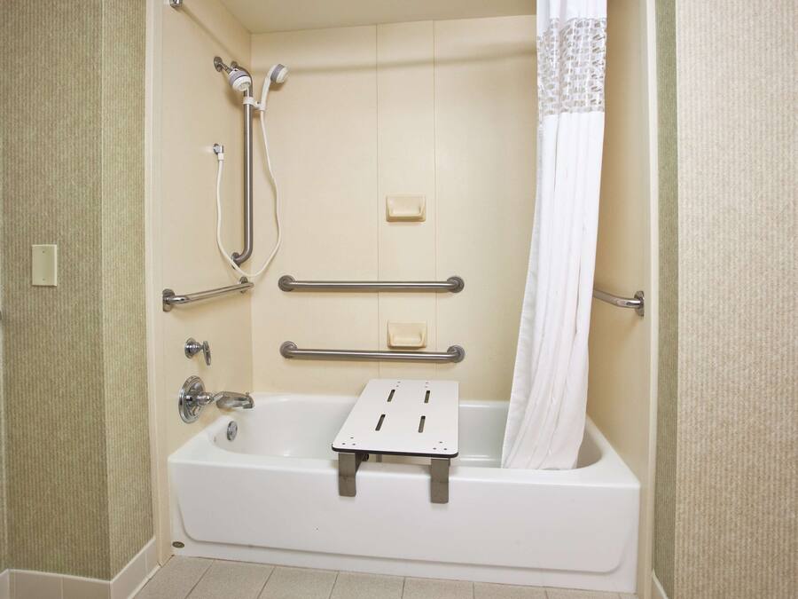 Une salle de bain équipée d’une baignoire, de barres d’appui, d’un pommeau de douche et d’un rideau de douche.