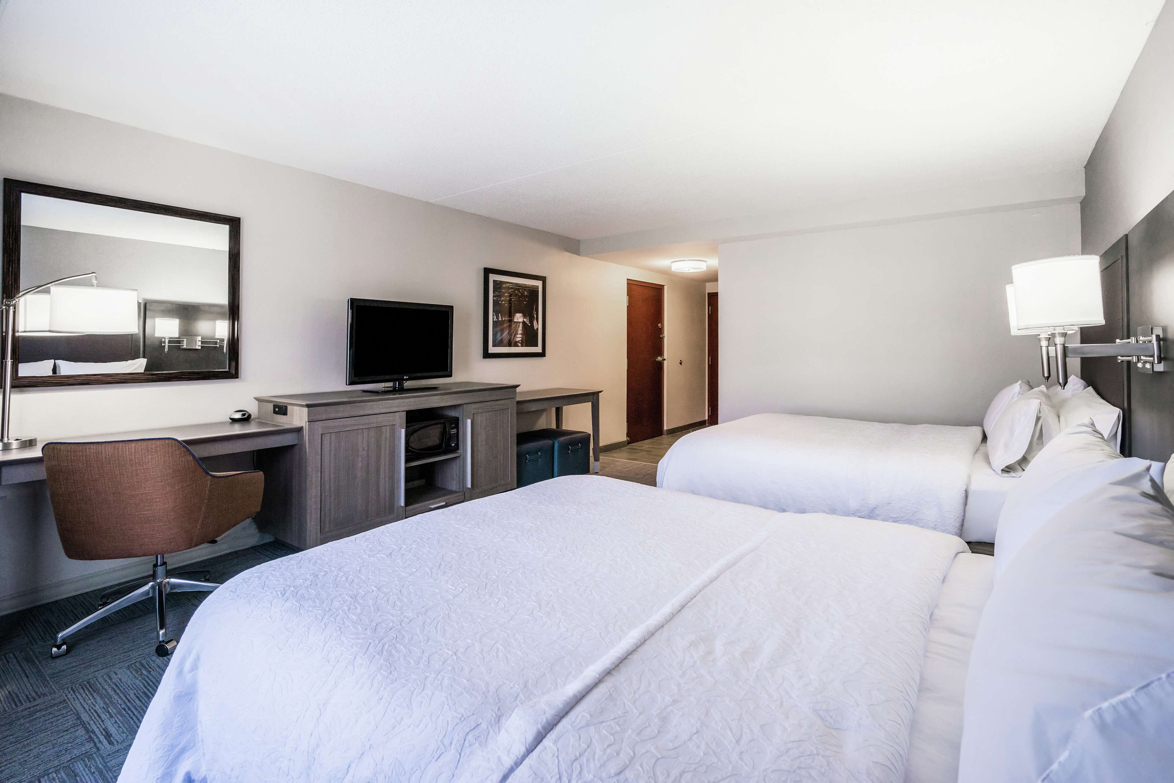 A hotel room with two beds, a desk with a chair, a television, and a mirror.
