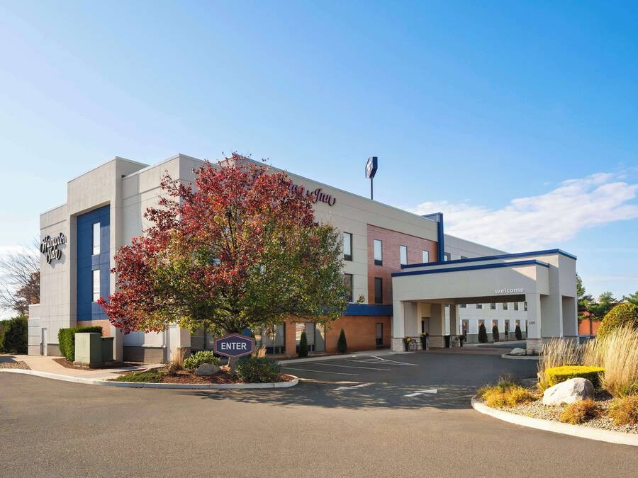 A modern hotel with a prominent entrance, a large tree with autumn foliage, and a clear blue sky.