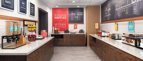 A modern kitchen area with a central counter, various food items, and a large chalkboard with writing.