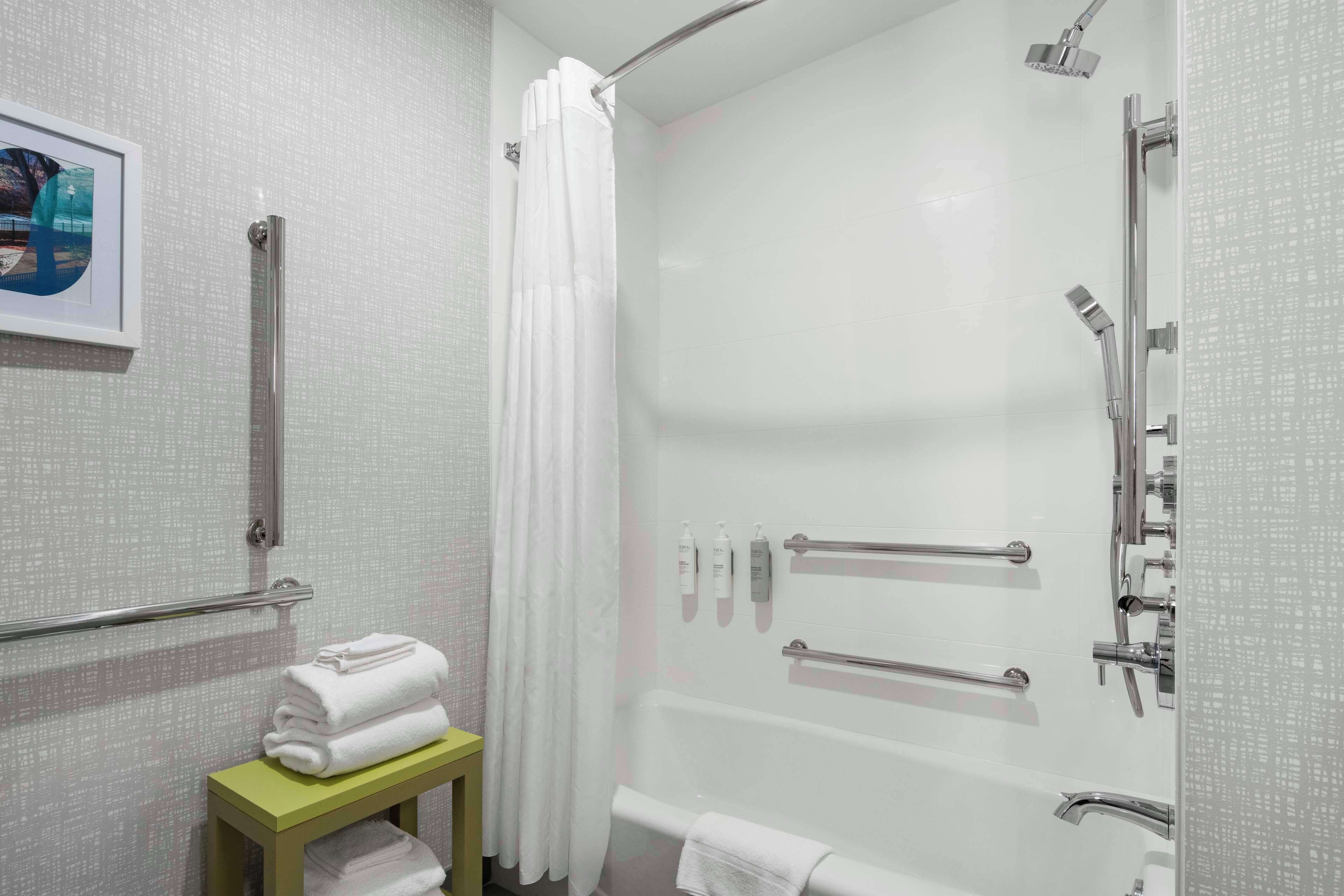 A modern bathroom with a walk-in shower, grab bars, a toilet with a safety bar, and a small table with towels.