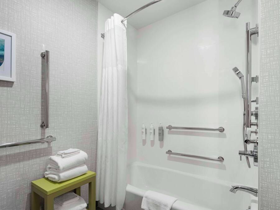 A modern bathroom with a walk-in shower, grab bars, a toilet with a safety bar, and a small table with towels.
