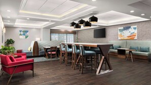 A modern hotel lobby with a dining area, seating, and a TV screen on the wall. - Hampton Inn Chicopee/Springfield (Chicopee)