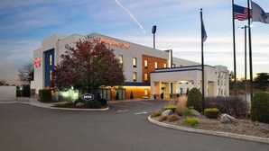 A Hampton Inn hotel with a modern design, featuring a large entrance, a well-lit parking area, and multiple flags. - Hampton Inn Chicopee/Springfield (Chicopee)