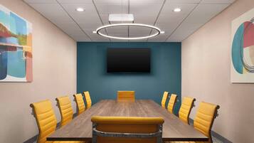 A conference room with a wooden table, yellow chairs, a mounted TV, and a ceiling light fixture.