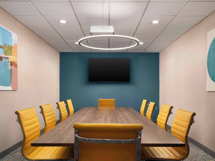 Ein Konferenzraum mit Holztisch, gelben Stühlen, einem Wand-Fernseher und einer Deckenleuchte.