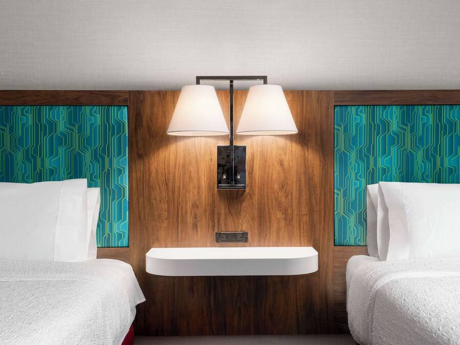A hotel room with two beds, a wooden accent wall, and a built-in sink.