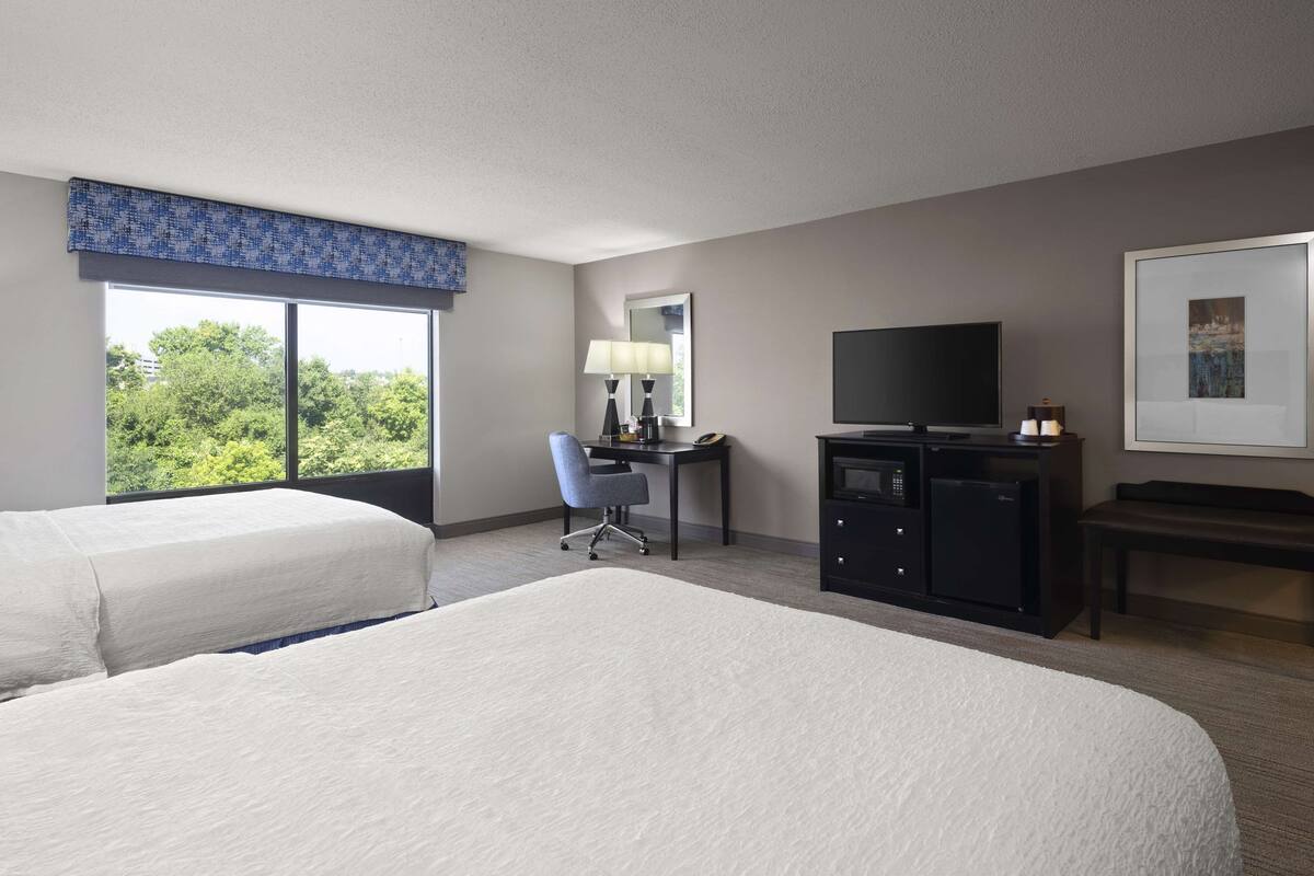 A hotel room with two beds, a desk with a chair, a television, a microwave, and a framed picture on the wall.