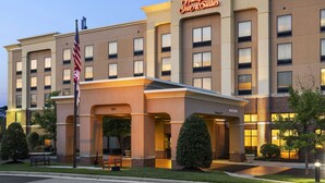 Un hôtel Hampton Inn & Suites au design architectural classique, avec un drapeau américain bien visible et une entrée accueillante.