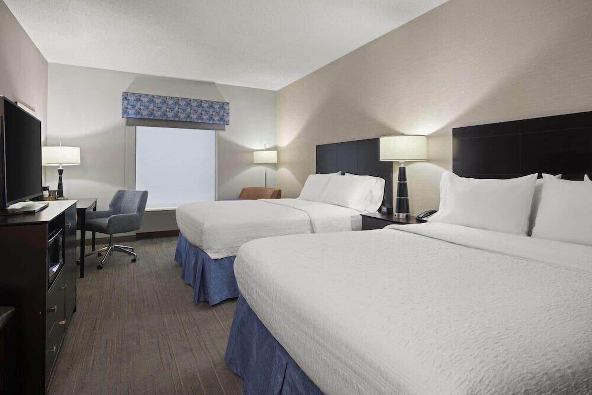 A hotel room with two beds, a desk with a TV, a chair, and a window with a view.