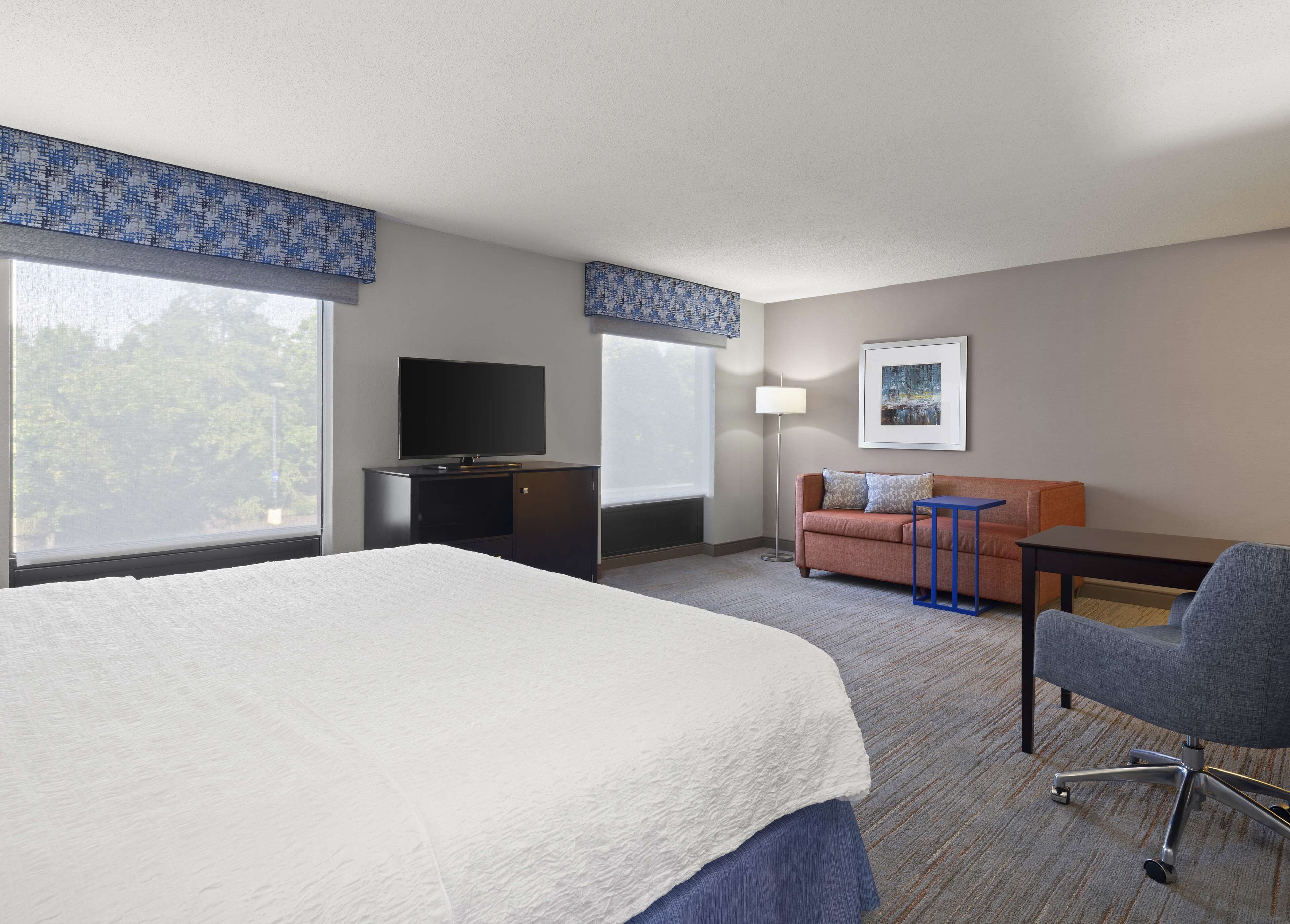 A hotel room with a large bed, a TV on a cabinet, a sofa, a desk, and a chair.