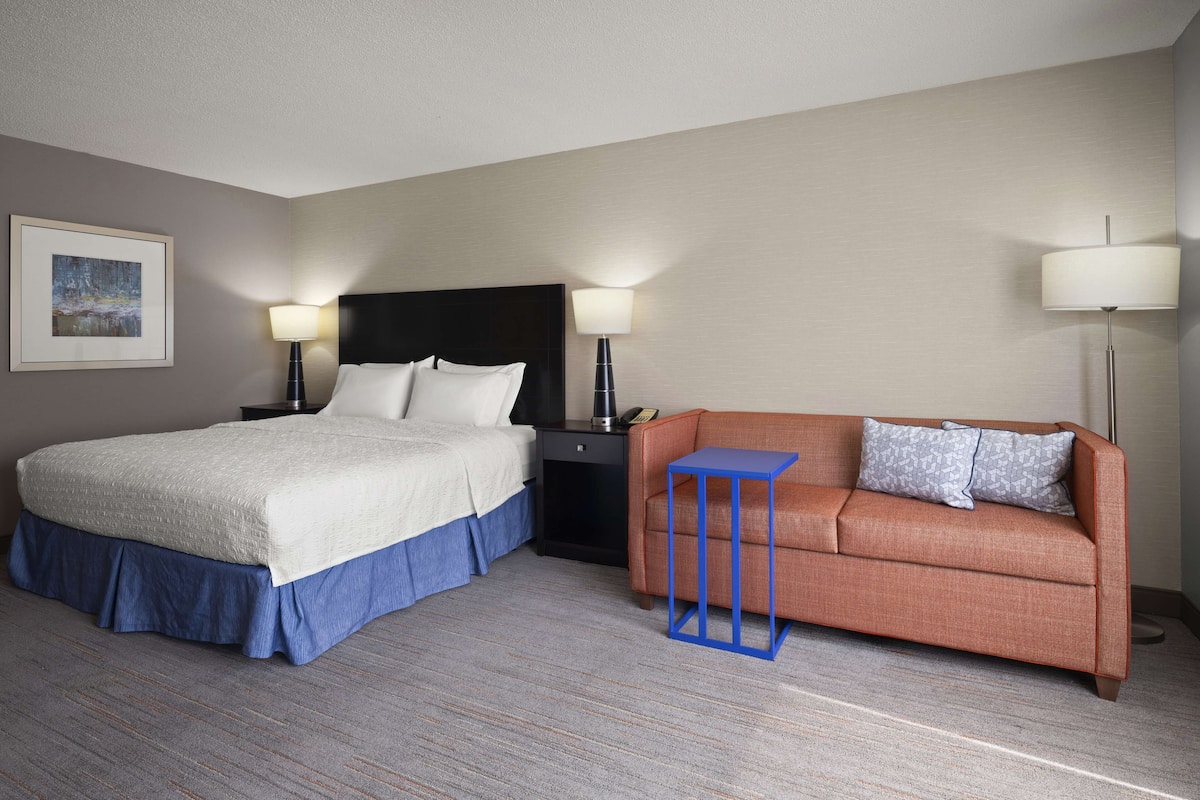 A hotel room with a bed, a sofa, a small table, and two bedside lamps.
