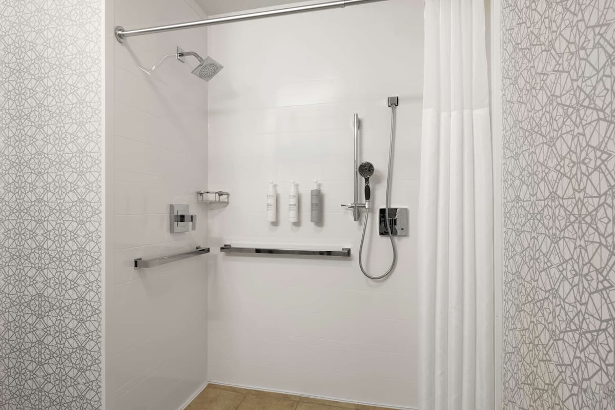 A modern shower area with a handheld showerhead, a wall-mounted showerhead, and a handheld shower head. There is a grab bar installed for safety.